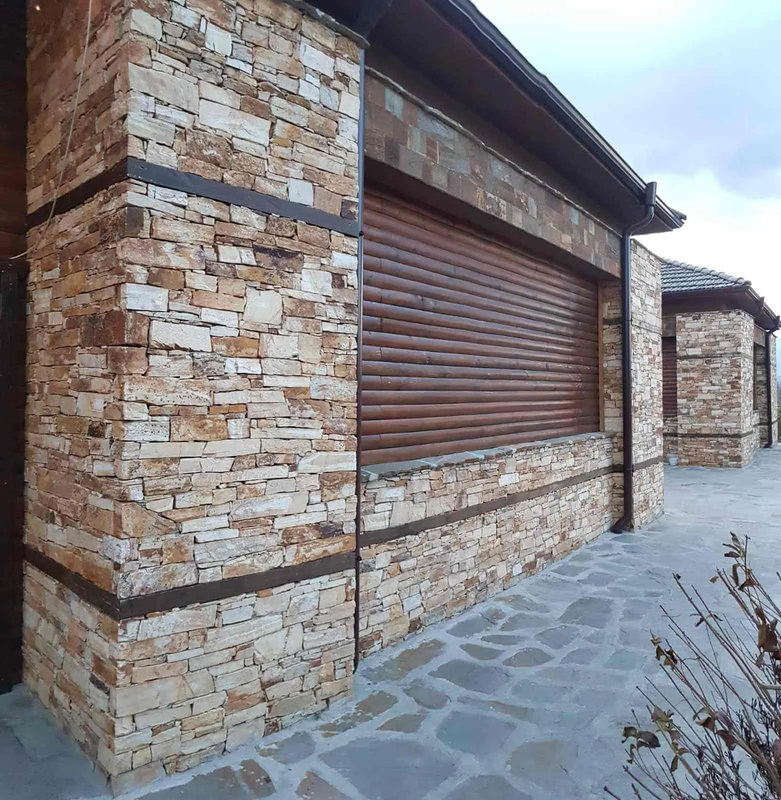 Rustic house facade with dry-stacked gneiss stone and irregular flagstone paving