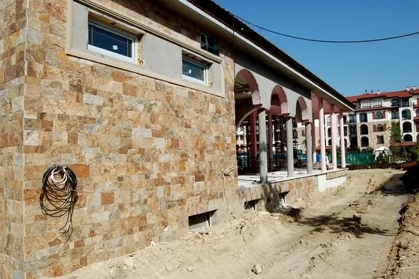 Hotel building facade with rectangular cut stone cladding and arched colonnade under construction