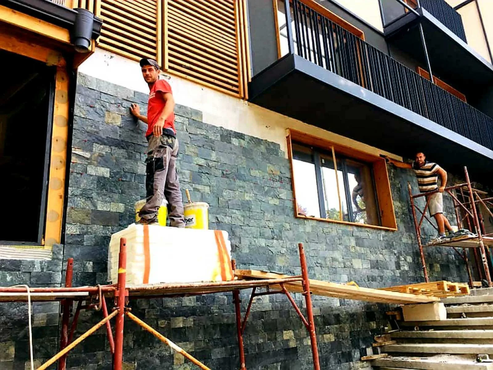 Workers installing cut green gneiss tiles on a house facade