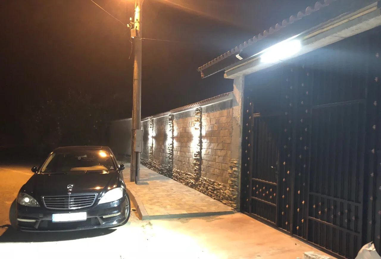 Illuminated stone-clad fence wall and metal gate at night