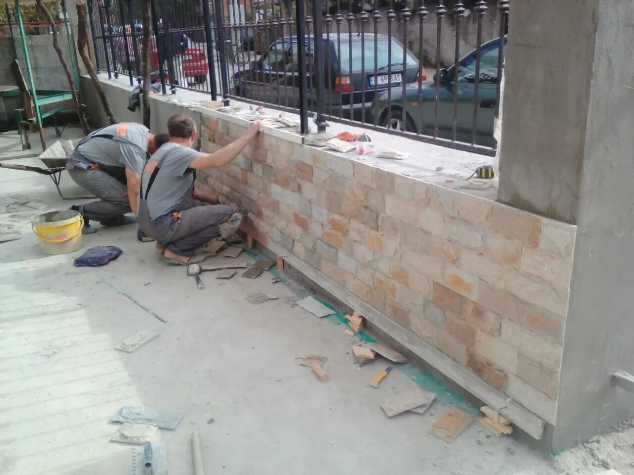 Workers installing rectangular cut stone tiles on a fence base