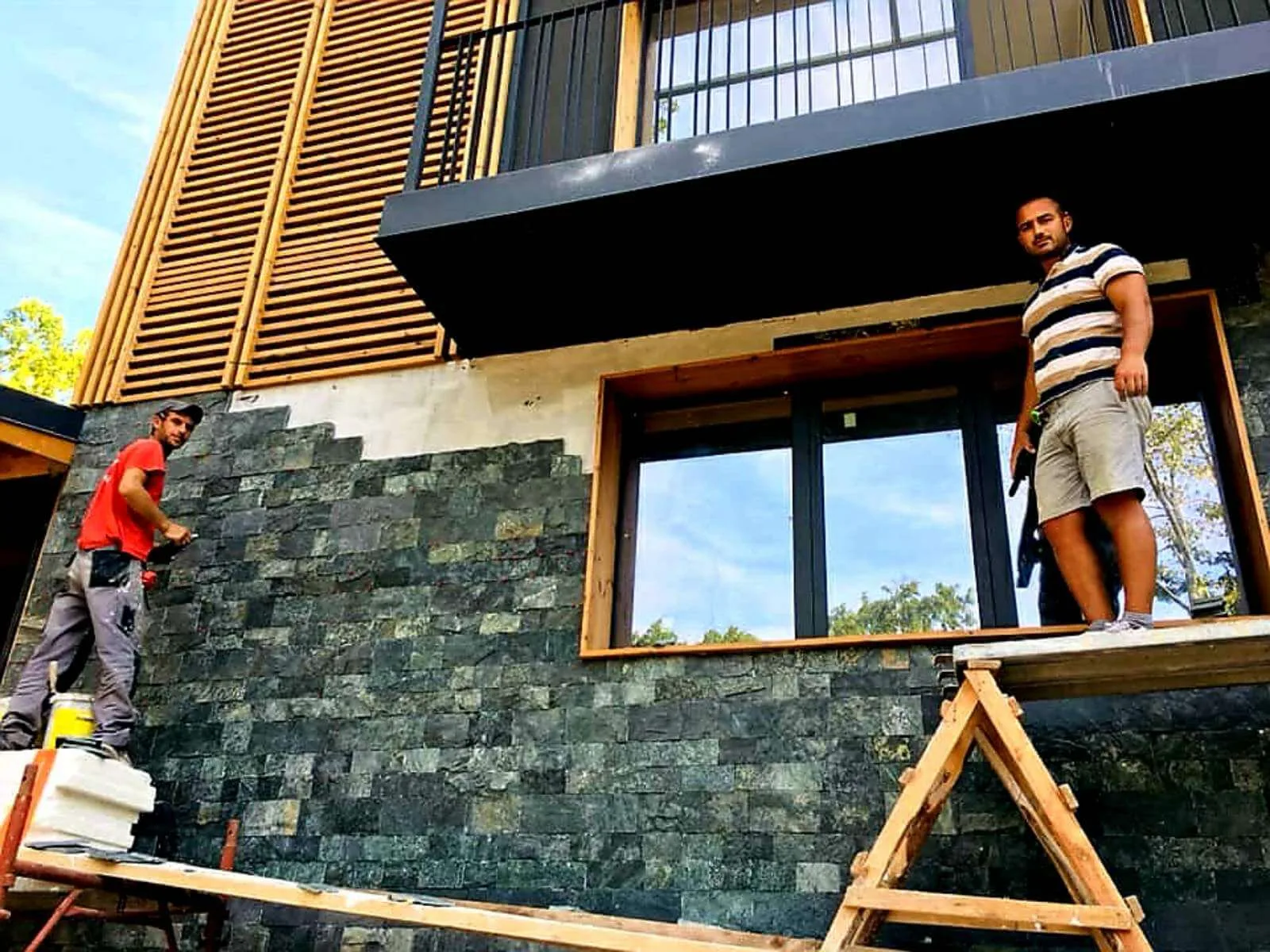 Workers on scaffolding installing green cut stone cladding around a window