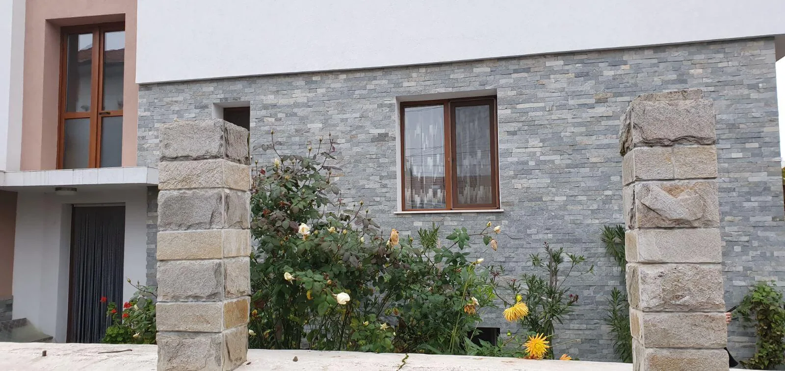 House facade with gray cut stone strips and rough stone fence pillars