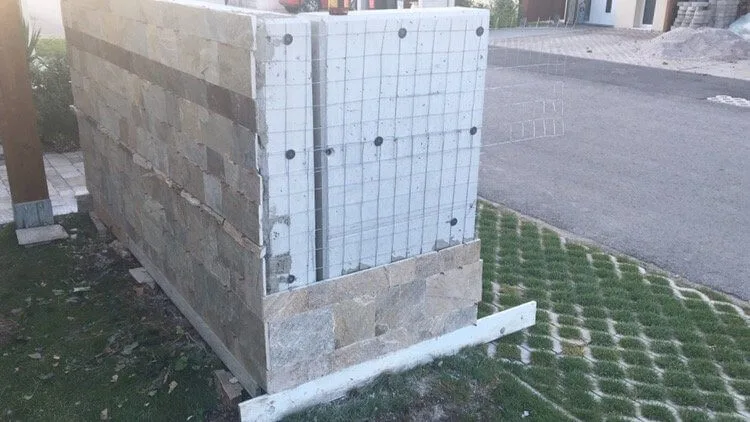 Fence wall clad with rectangular cut stone tiles during construction