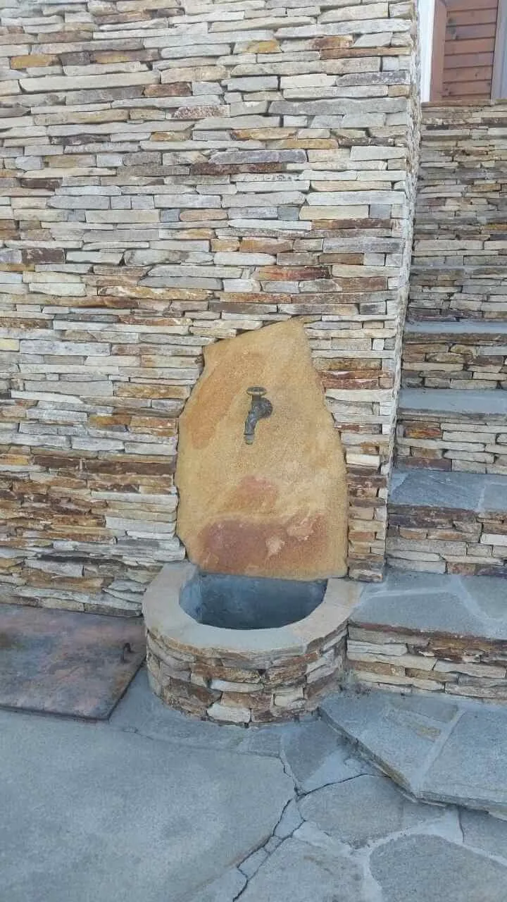 Stone garden fountain with brass tap set against a stacked stone wall