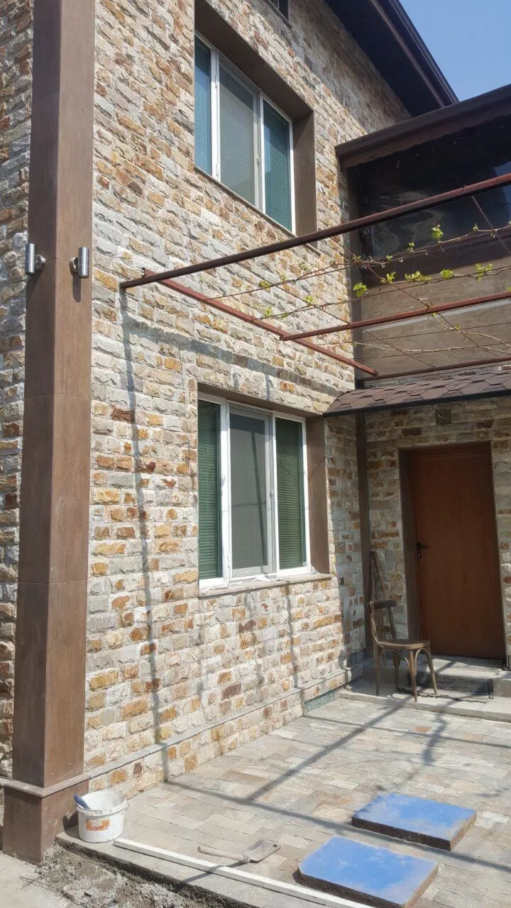 Two-storey house facade with rustic natural stone veneer and pergola
