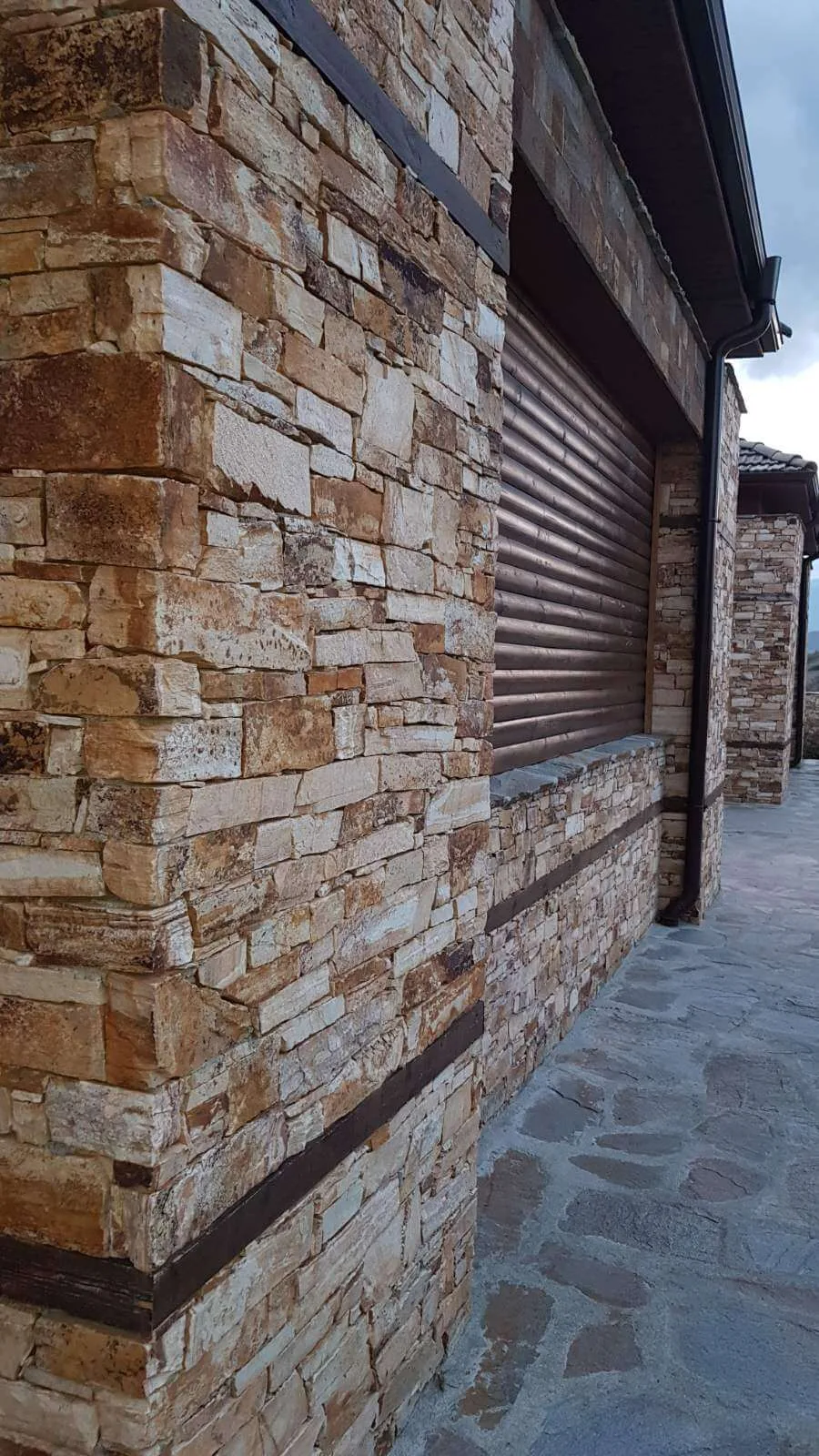 Close-up of dry-stacked gneiss stone facade with copper roller shutter