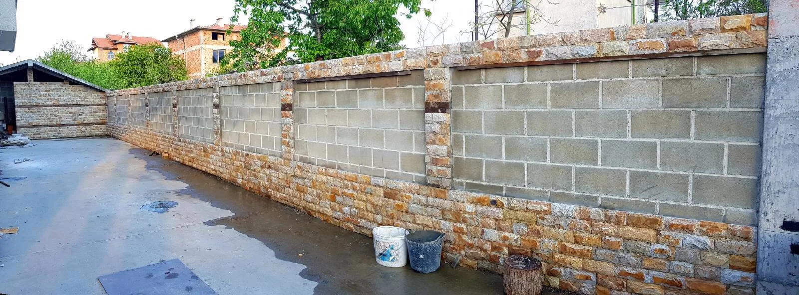 Yard fence wall being clad with cut gneiss stone around concrete blocks