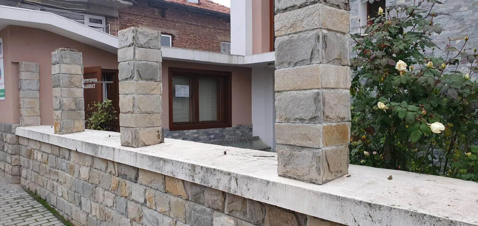 Stone fence with rubble masonry wall and cut stone pillars by a sidewalk