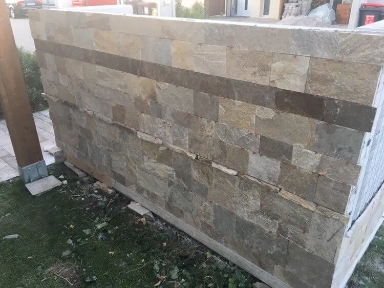 Fence wall clad with rectangular cut stone tiles during installation