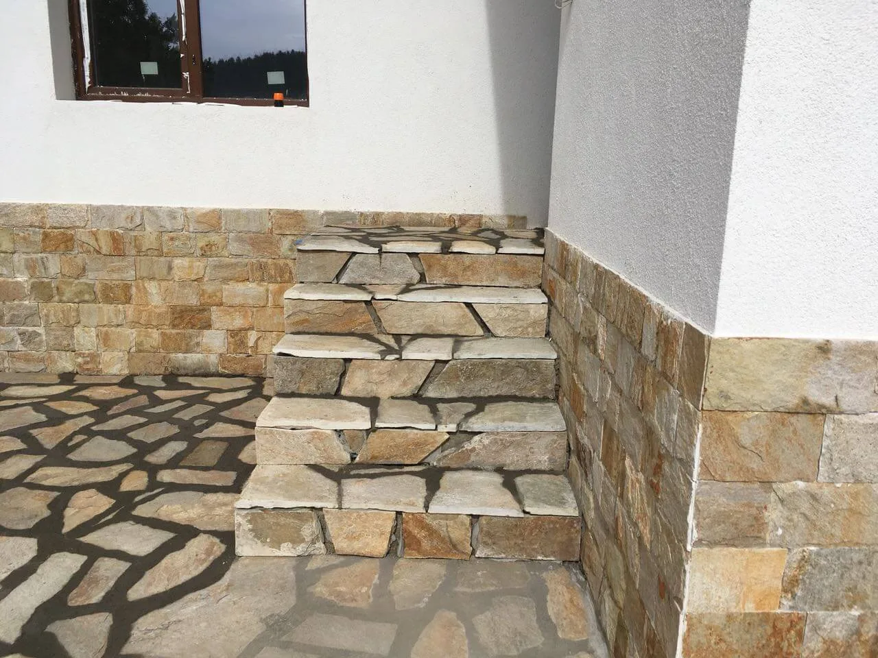 Stone steps and polygonal flagstone paving beside a stone-clad wall base
