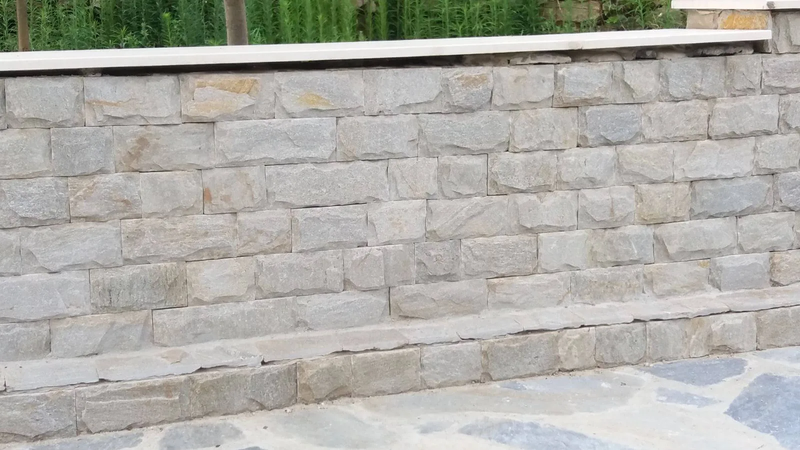 Garden wall built with cut grey gneiss blocks and light stone coping