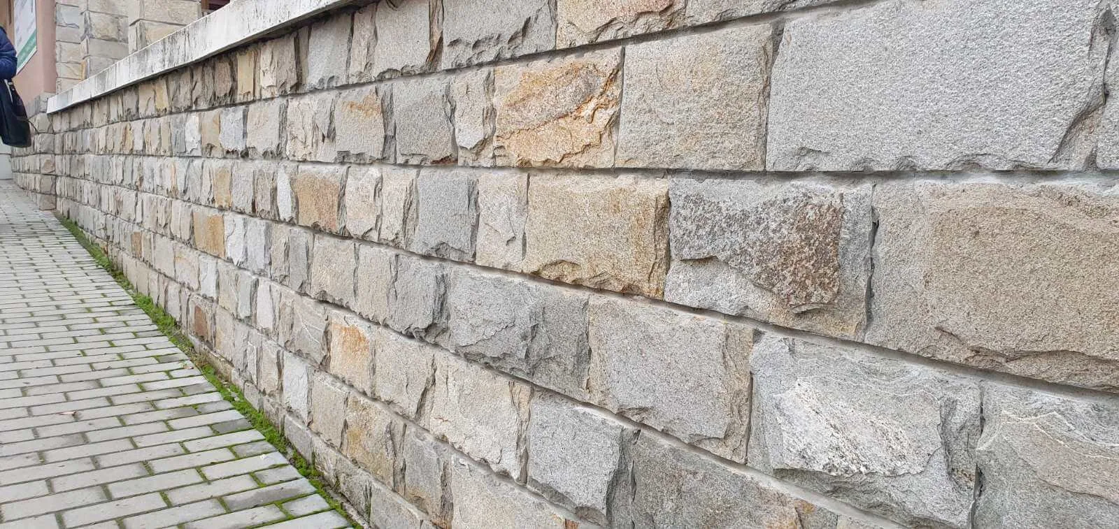 Street retaining wall faced with cut gneiss blocks along a paved sidewalk
