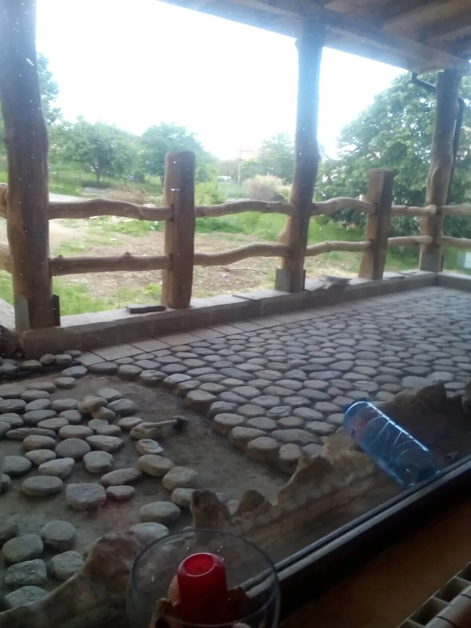 Covered terrace paved with round river pebbles and a rustic wooden railing