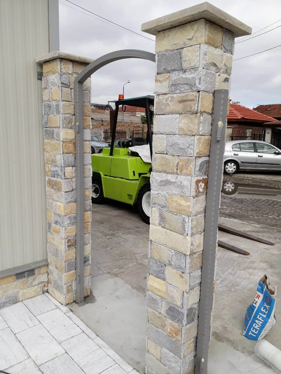 Entrance gate pillars clad with multicoloured cut stone blocks under a metal arch