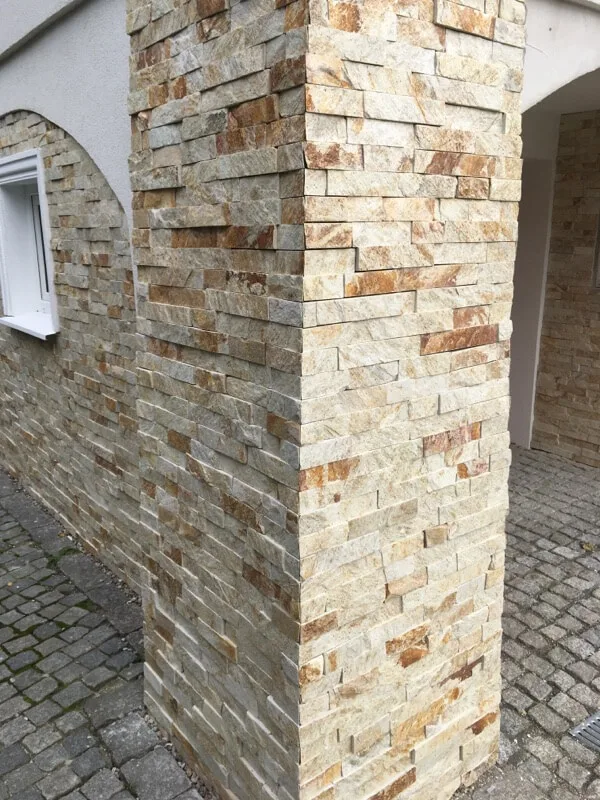 Column and wall clad with beige stacked stone strips beside a cobbled path