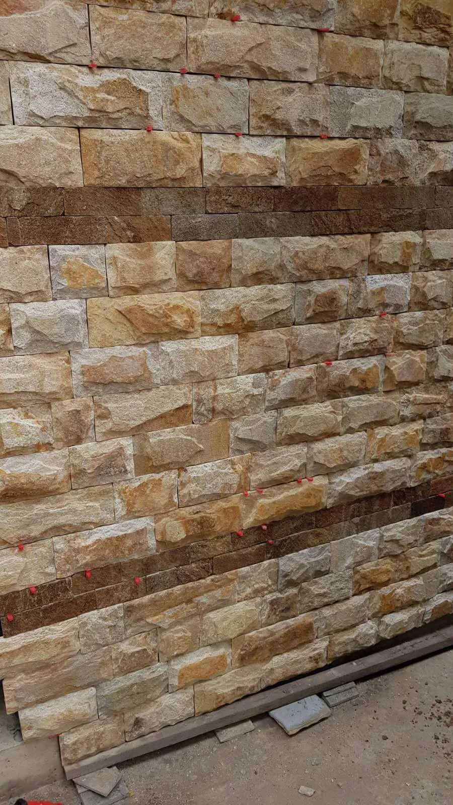 Wall being clad with rock-face cut gneiss blocks in warm beige tones