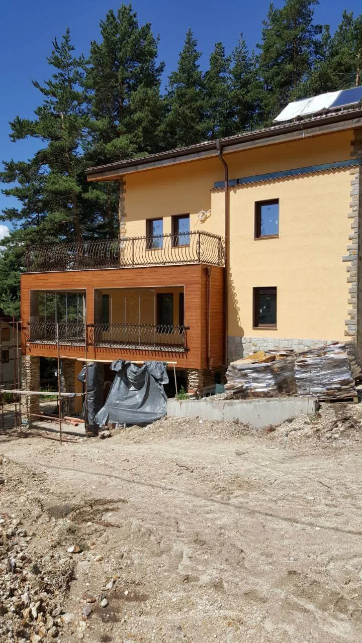 House under construction with stone-clad pillars and pallets of gneiss flagstones