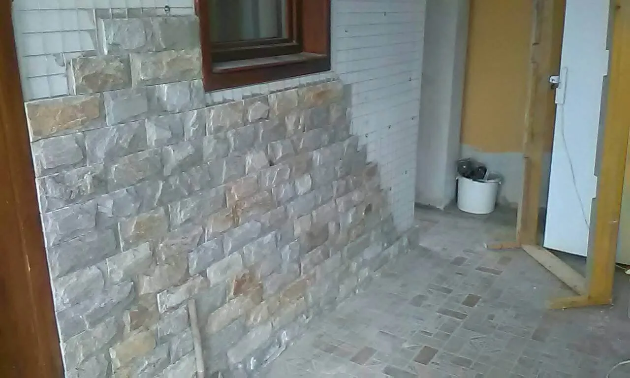 House wall being clad with cut gneiss stone pieces around a wooden window