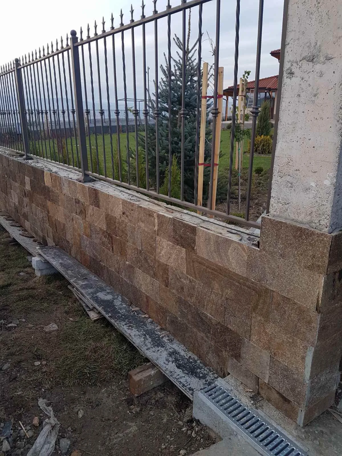Fence base clad with brown cut gneiss strips beneath a wrought-iron railing