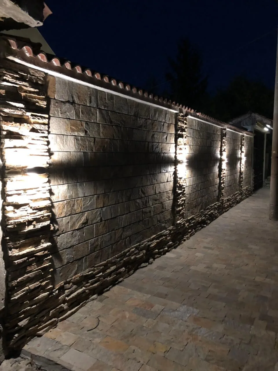 Stone fence wall with cut strips and stacked pillars illuminated at night