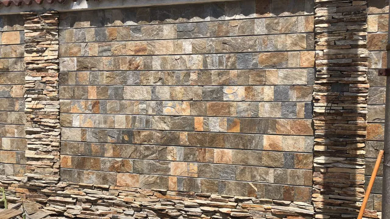Fence wall clad with rustic cut gneiss rectangles and stacked stone pillars
