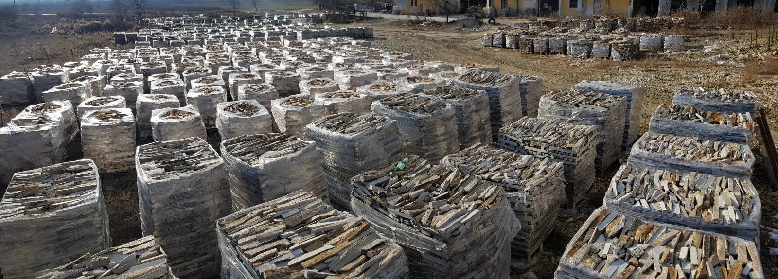 Rows of foil-wrapped pallets loaded with gneiss stone strips at the stone yard.