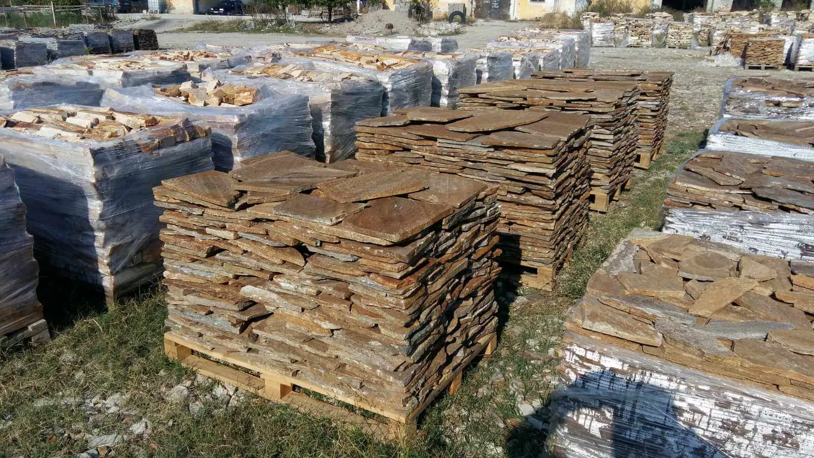 Stone yard with pallets of stacked brown gneiss flagstones.