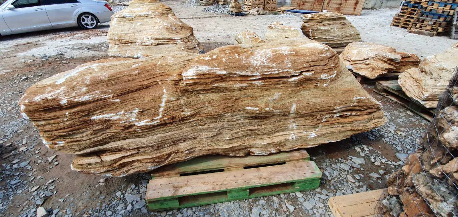 Massive striped gneiss boulders on pallets in the stone yard.