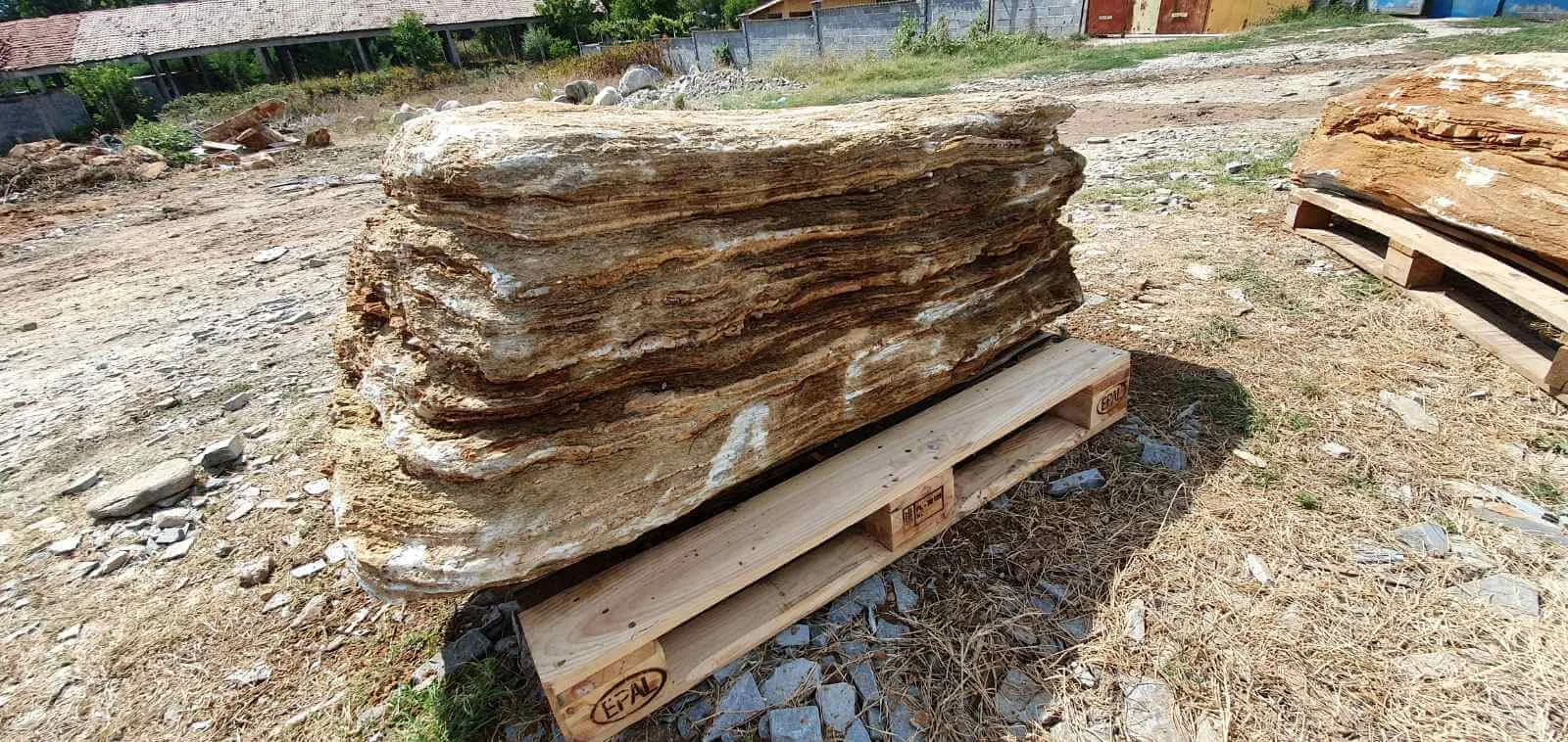 Large layered gneiss monolith on a wooden pallet at the storage yard.