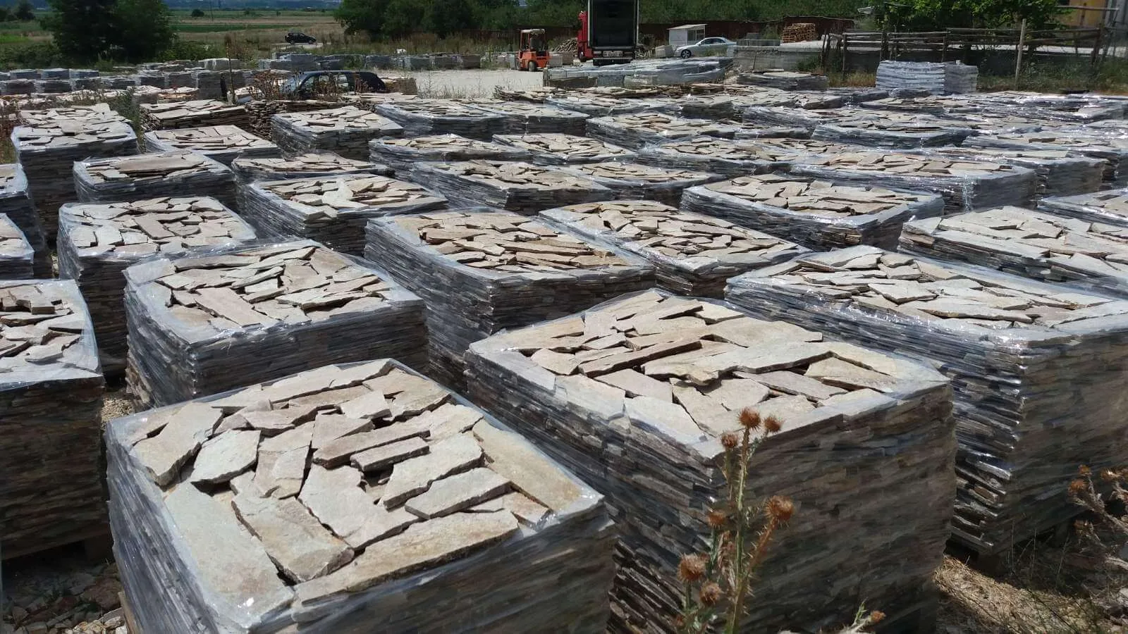 Yard full of foil-wrapped pallets stacked with beige gneiss flagstones.