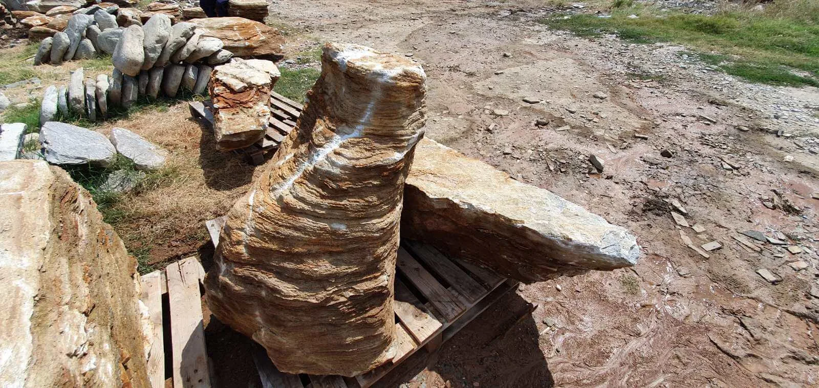 Sculptural layered gneiss boulder on a pallet surrounded by rubble stone.