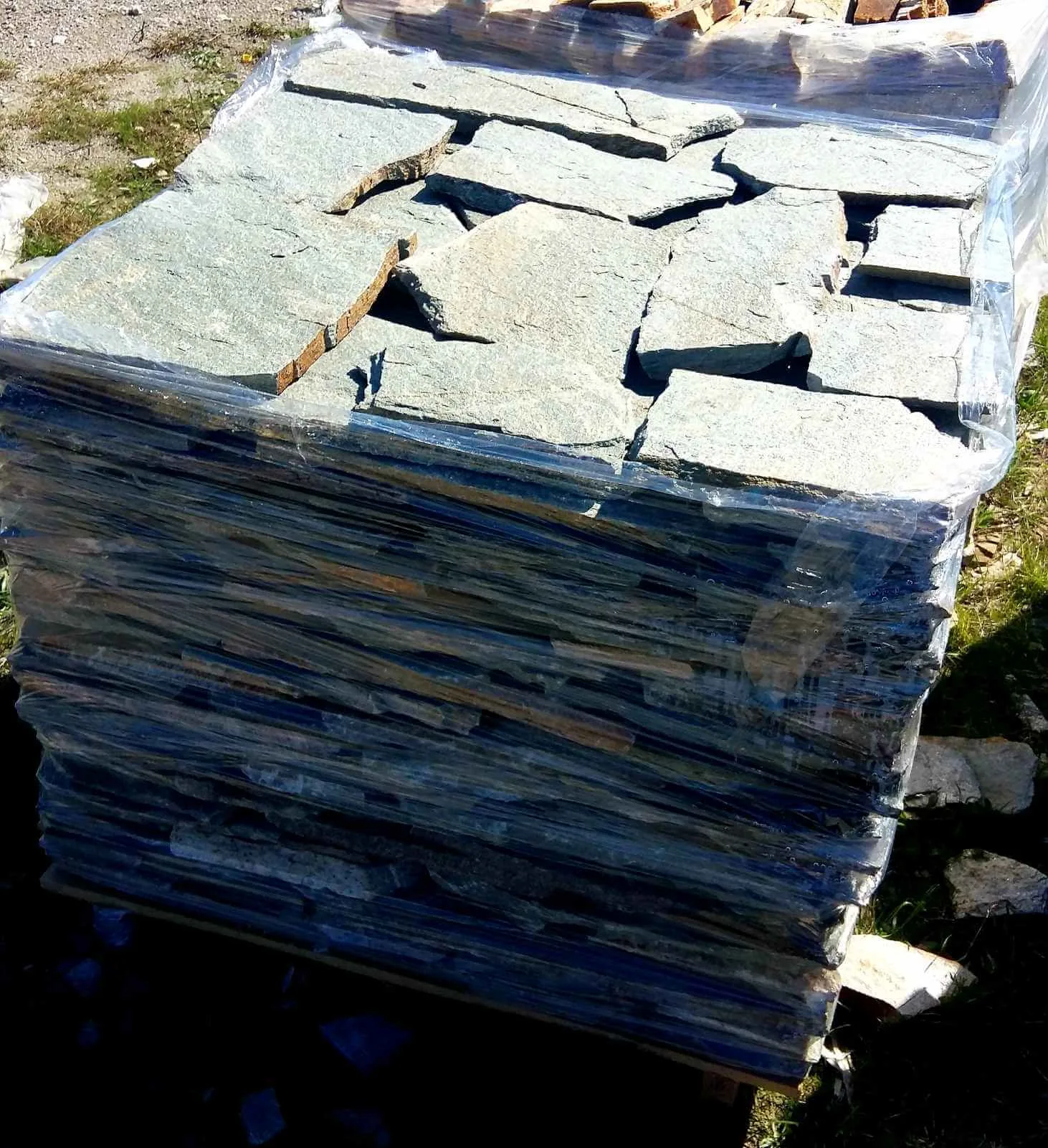 Foil-wrapped pallet of grey irregular gneiss flagstones in the yard.