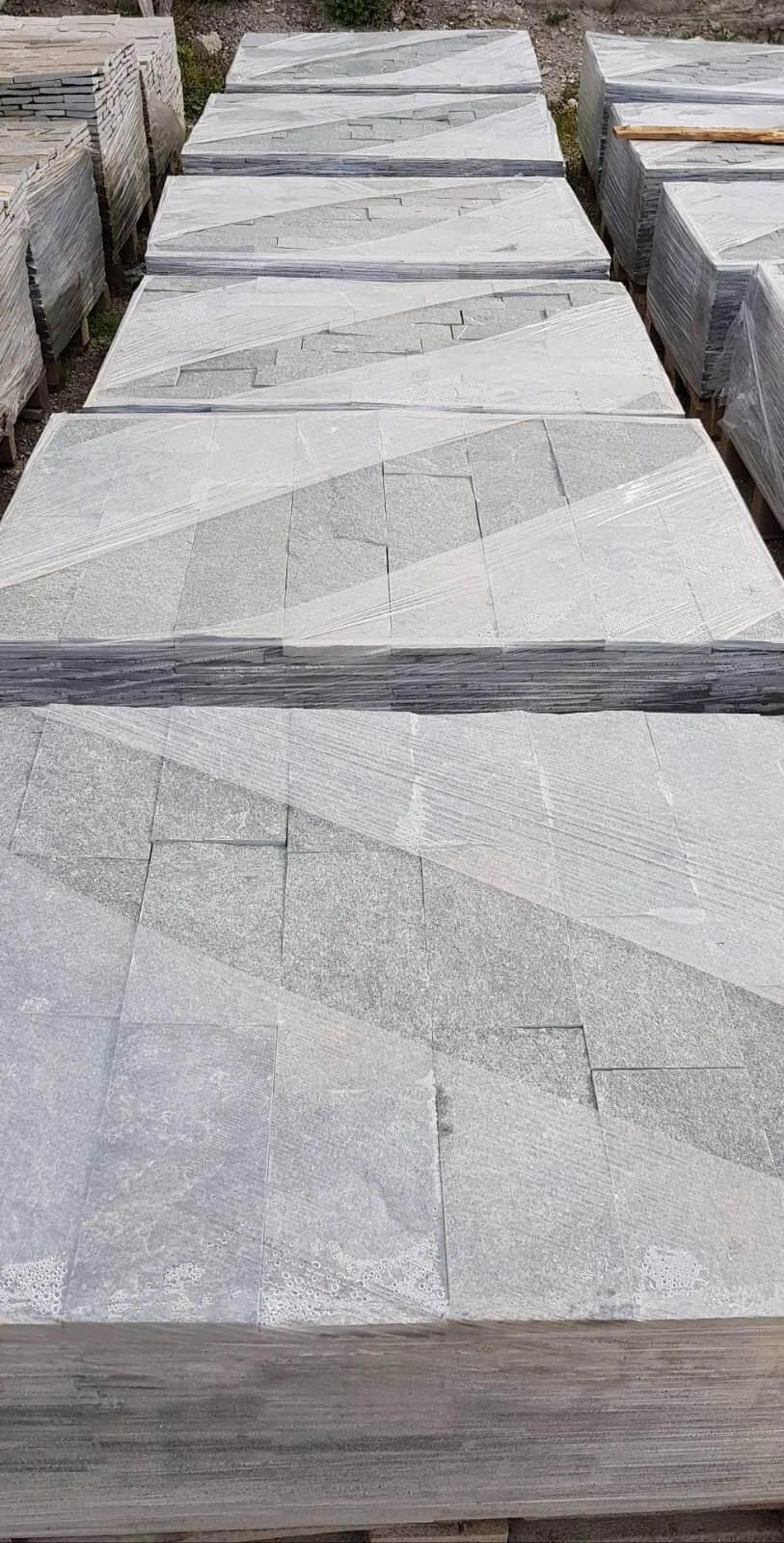 Rows of pallets with light grey sawn gneiss tiles ready for shipment