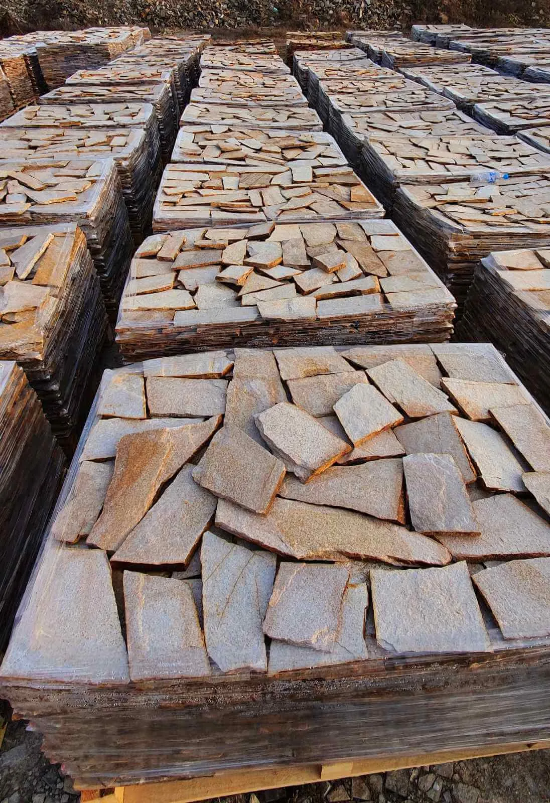 Rows of pallets stacked with irregular tan gneiss flagstones at the stone yard