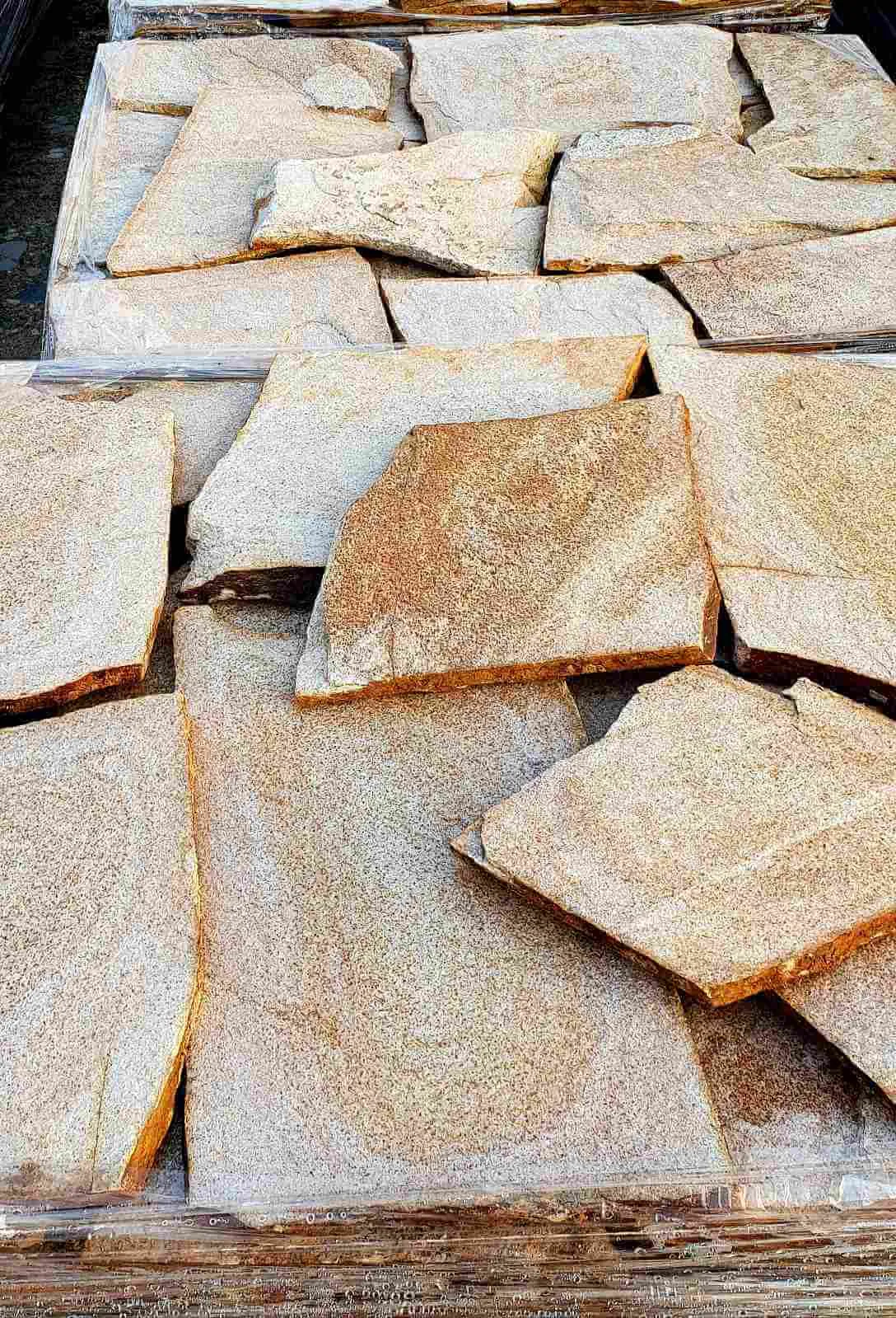 Close view of large sand-colored gneiss flagstone slabs stacked on a pallet