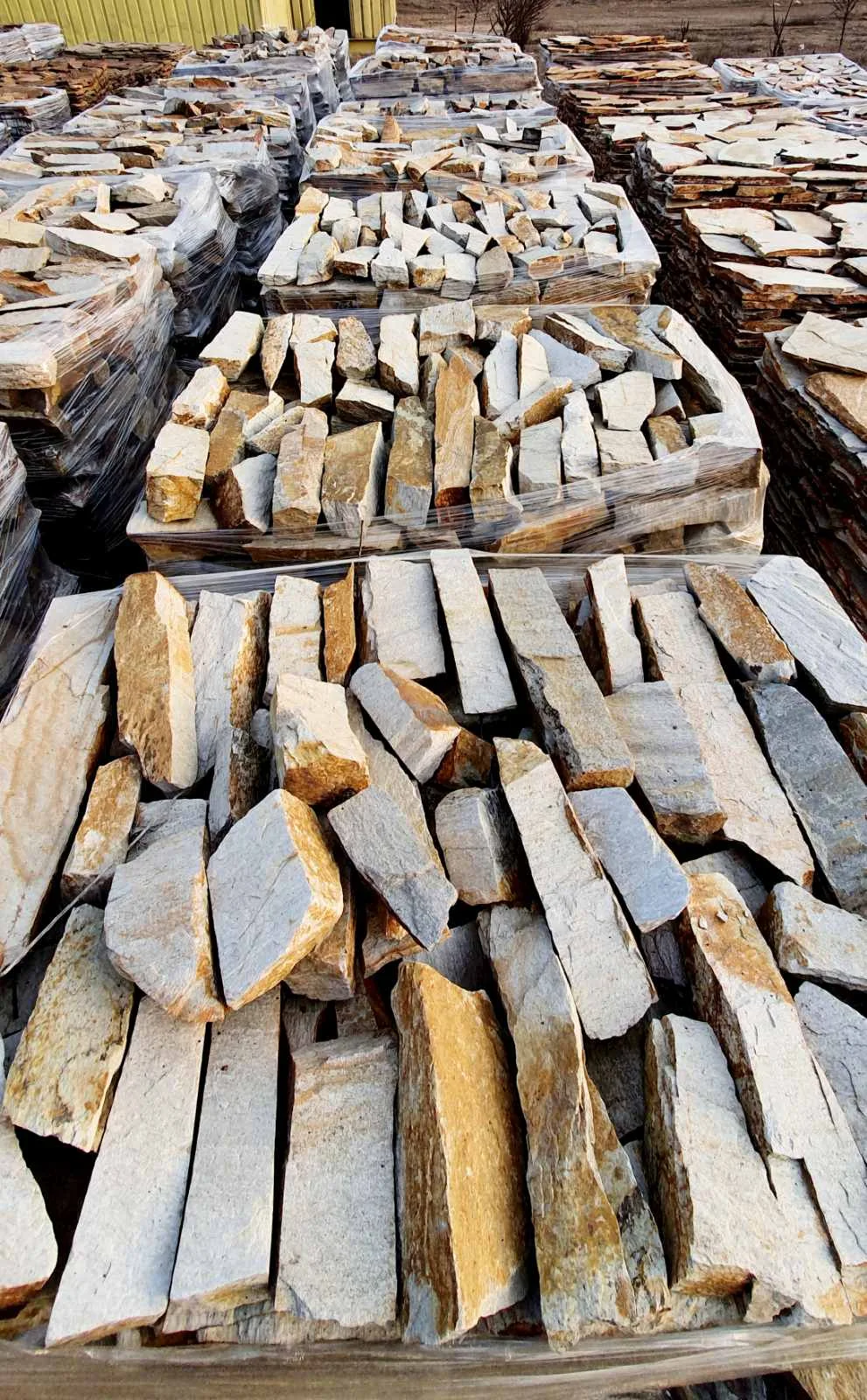 Stone yard with many pallets of cut gneiss strips and rubble pieces
