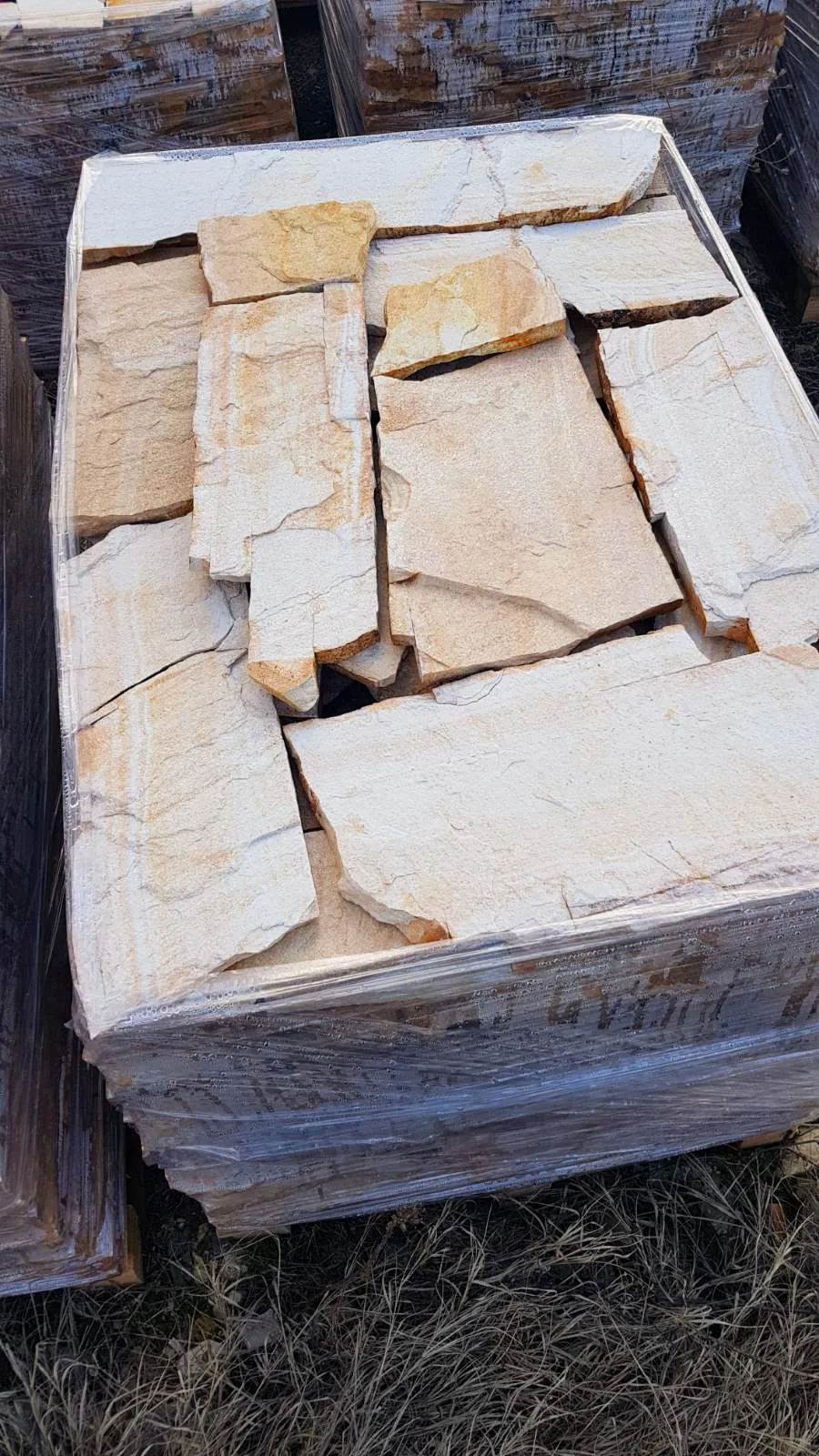 Pallet stacked with large cream-colored irregular gneiss flagstones