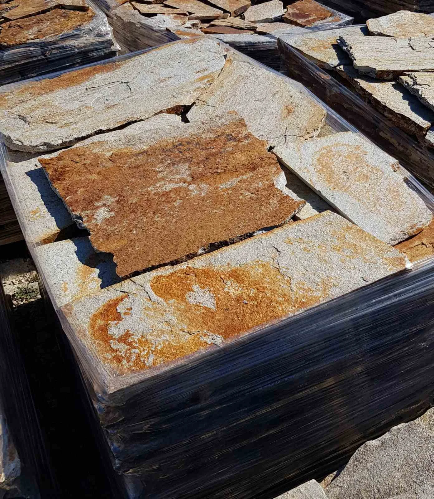 Pallet with large rust-toned gneiss flagstone slabs wrapped in foil