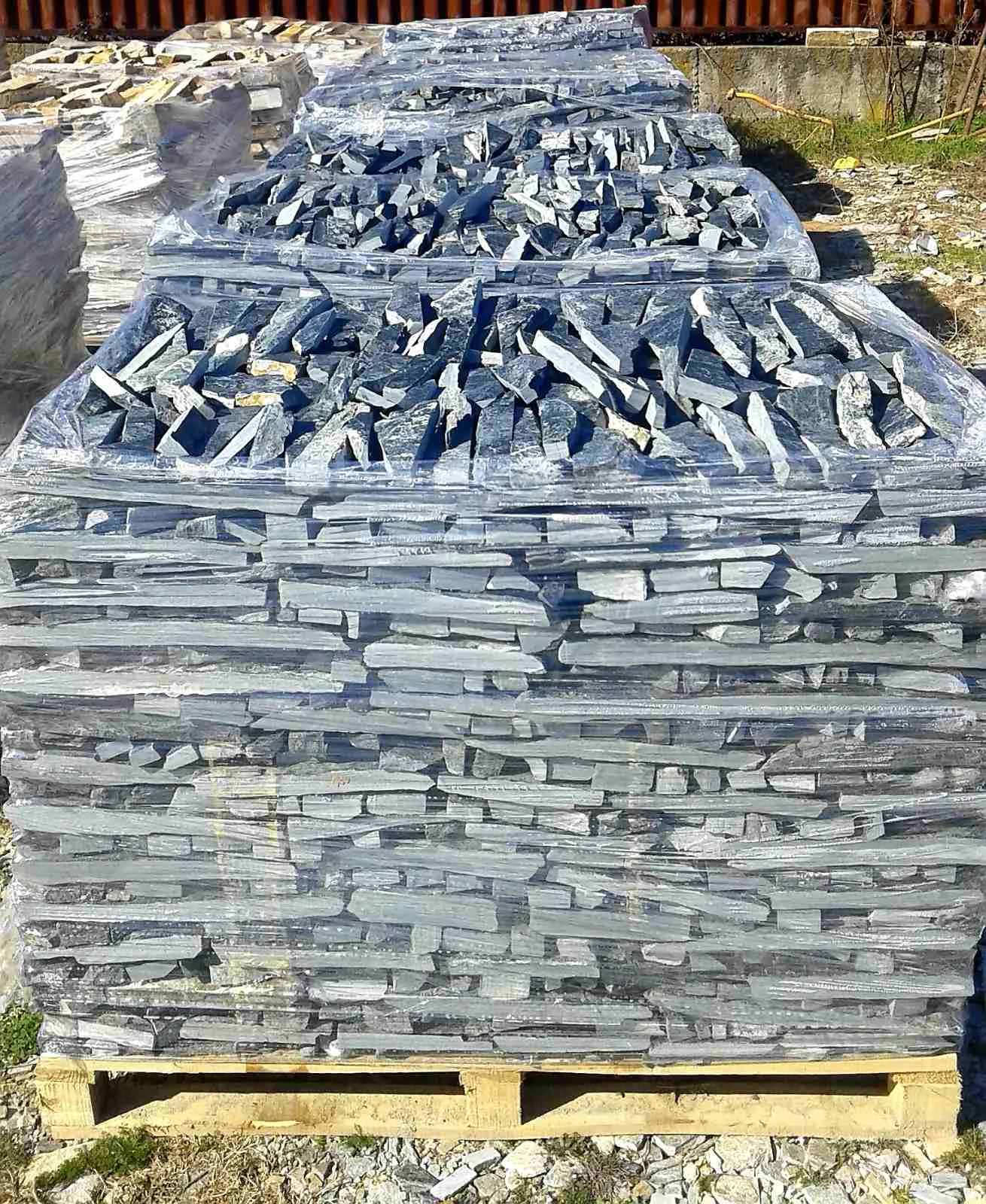 Stacked pallets of blue-gray gneiss wall stone strips at the yard
