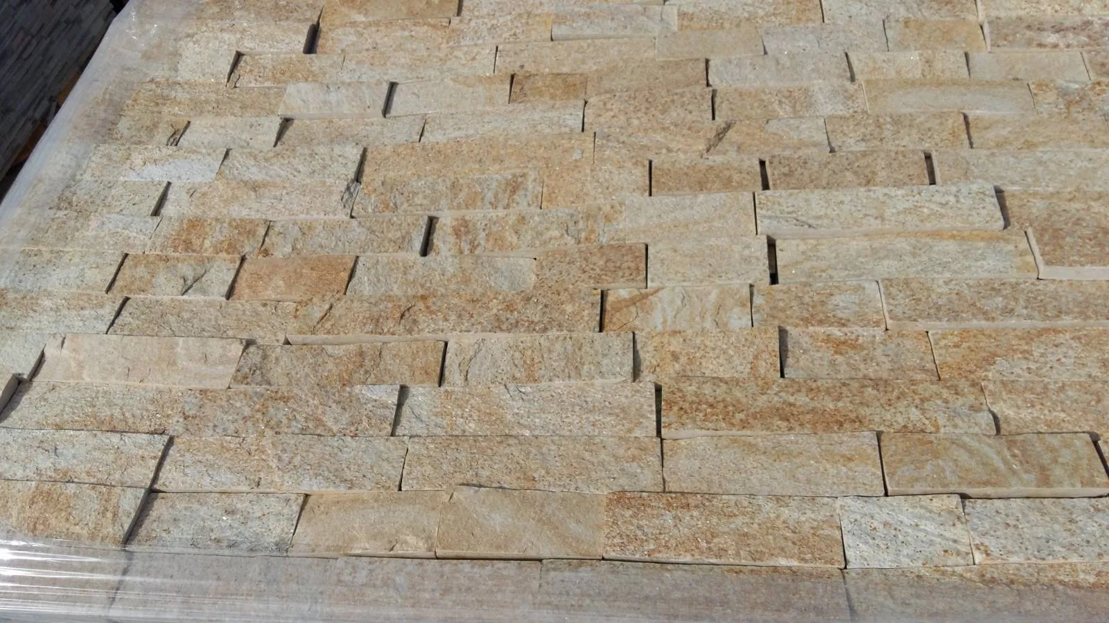 Close-up of beige split-face gneiss cladding strips on a pallet