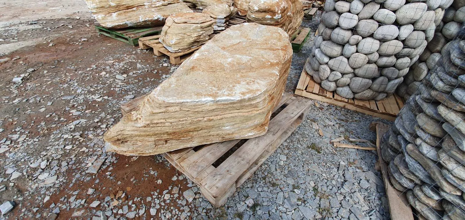 Decorative garden boulders and cages of rounded pebbles on pallets at the stone yard