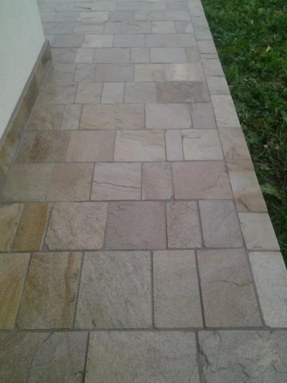 Terrace path paved with cut gneiss tiles in beige tones next to a lawn