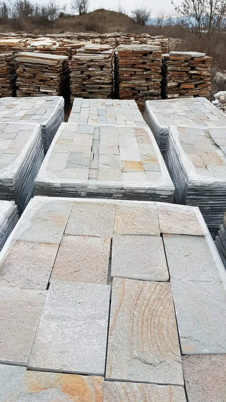 Pallets of square gneiss paving tiles with stacks of raw flagstone behind