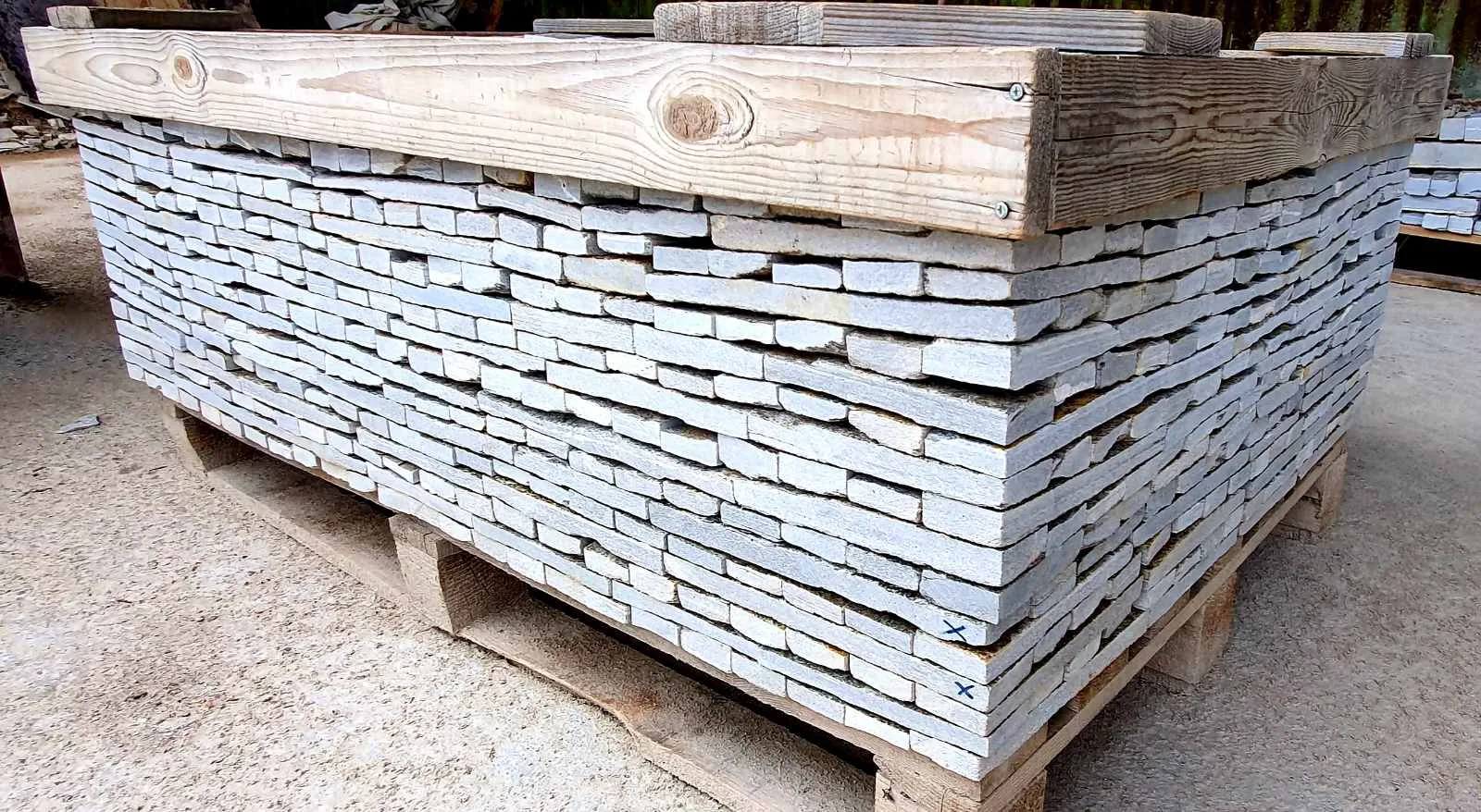 Wooden crate packed with thin gray cut gneiss strips on a pallet