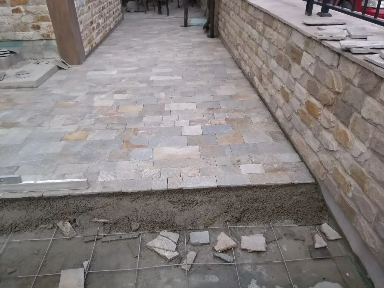 Courtyard paving with cut gneiss tiles being laid beside a stone-clad wall