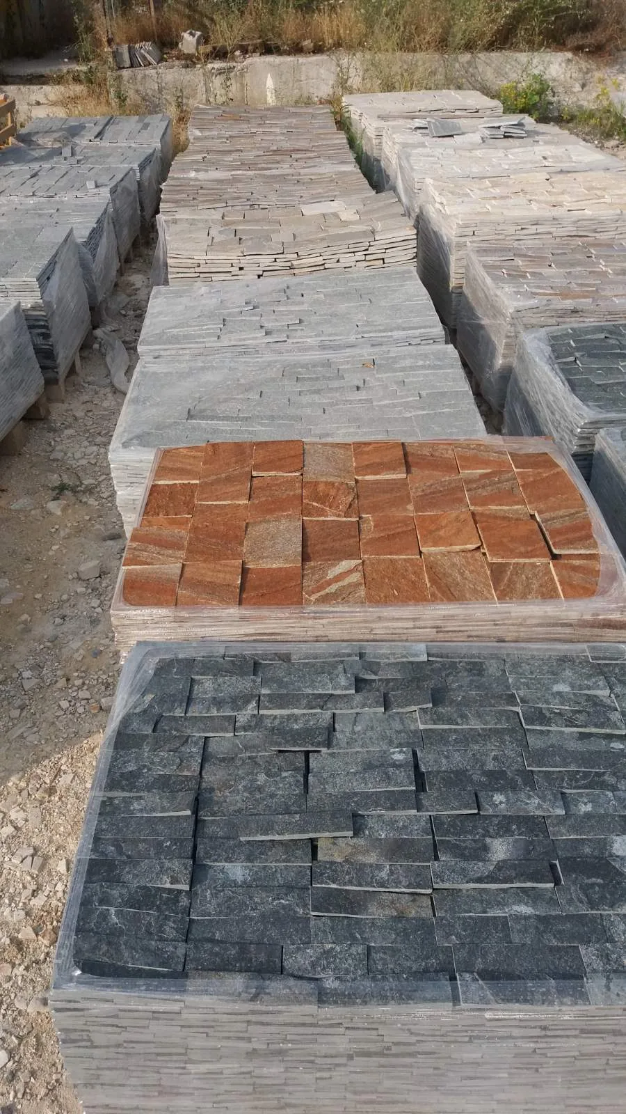 Stone yard with pallets of gray, rust and dark cut cladding tiles