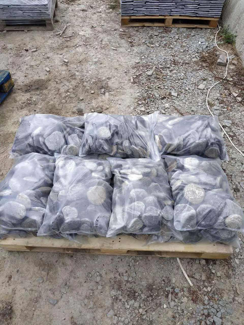 Plastic bags of rounded decorative pebbles on a wooden pallet