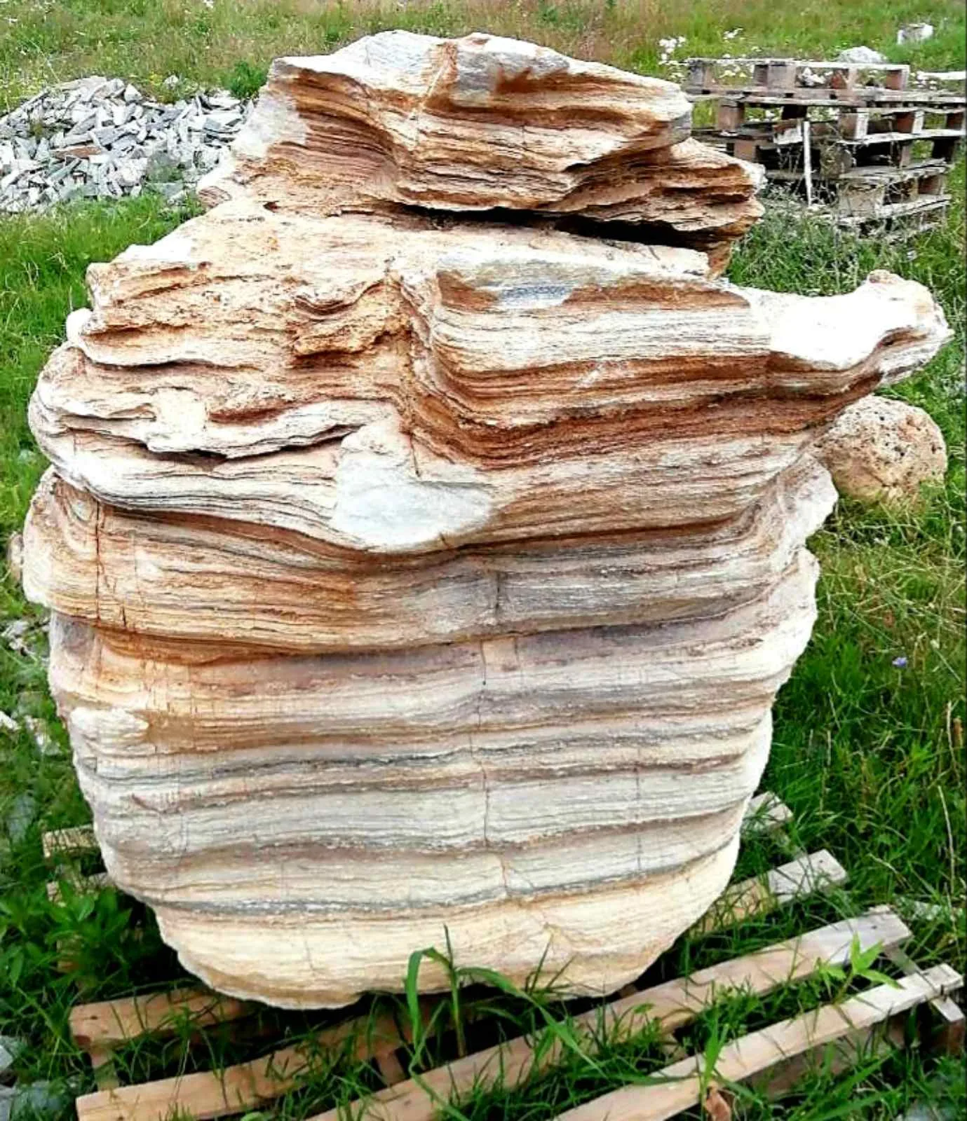 Massive layered decorative boulder standing on a pallet in the grass