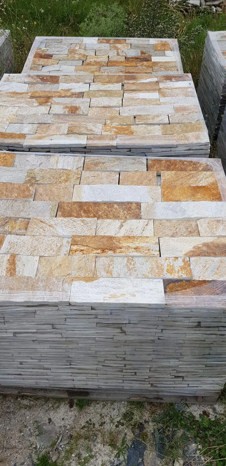 Pallets of beige cut gneiss cladding strips stacked at the yard